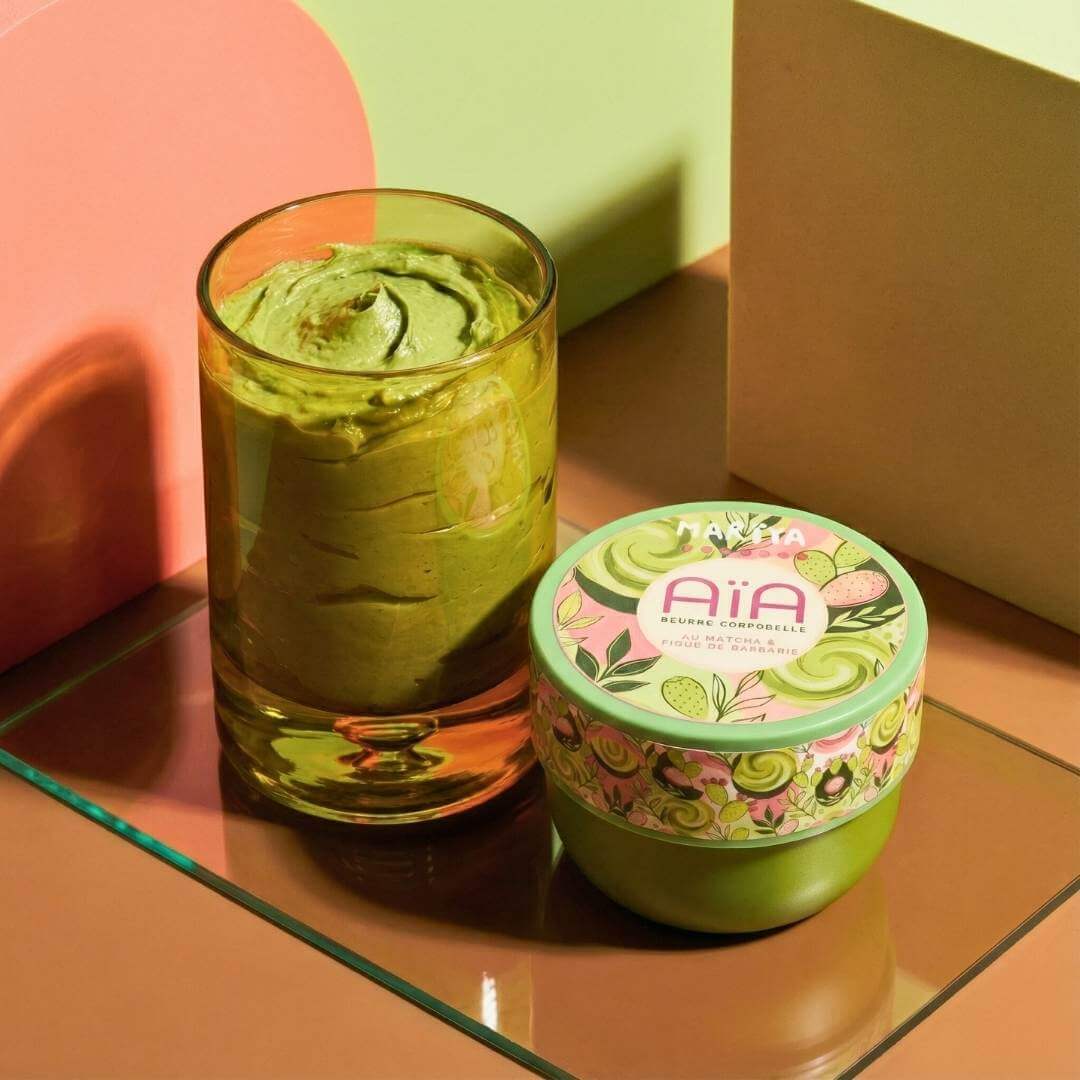 AÏA beurre corporel nourrissant au Matcha et Figue de Barbarie dans un pot sur table avec un verre de texture de beurre.