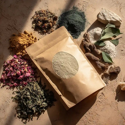 Pochette de poudre capillaire naturelle entourée d’ingrédients bruts – herbes, fleurs et épices – soins artisanaux marocains MARÏYA