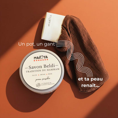 Pot artisanal du savon beldi MARÏYA posé à côté d’un gant kessa. Représente le rituel hammam marocain traditionnel, symbole de soin, de douceur et de transmission.