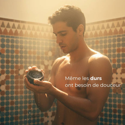 Un homme marocain au style rétro des années 70 dans la vapeur chaude du hammam.
Il rince le savon noir sur sa peau, la lumière dorée joue avec la brillance de l’eau et des carreaux.
Une scène cinématique, poétique et authentique, célébrant la beauté masculine marocaine et l’art du soin ancestral.