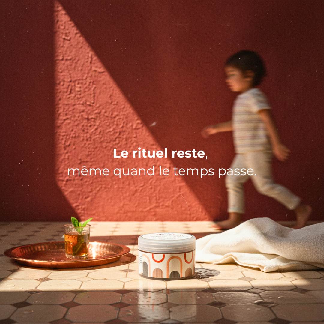 Pot de savon beldi MARÏYA posé au sol, avec un enfant passant derrière en mouvement. Image symbolique du rituel qui se transmet, entre tradition, tendresse et modernité.