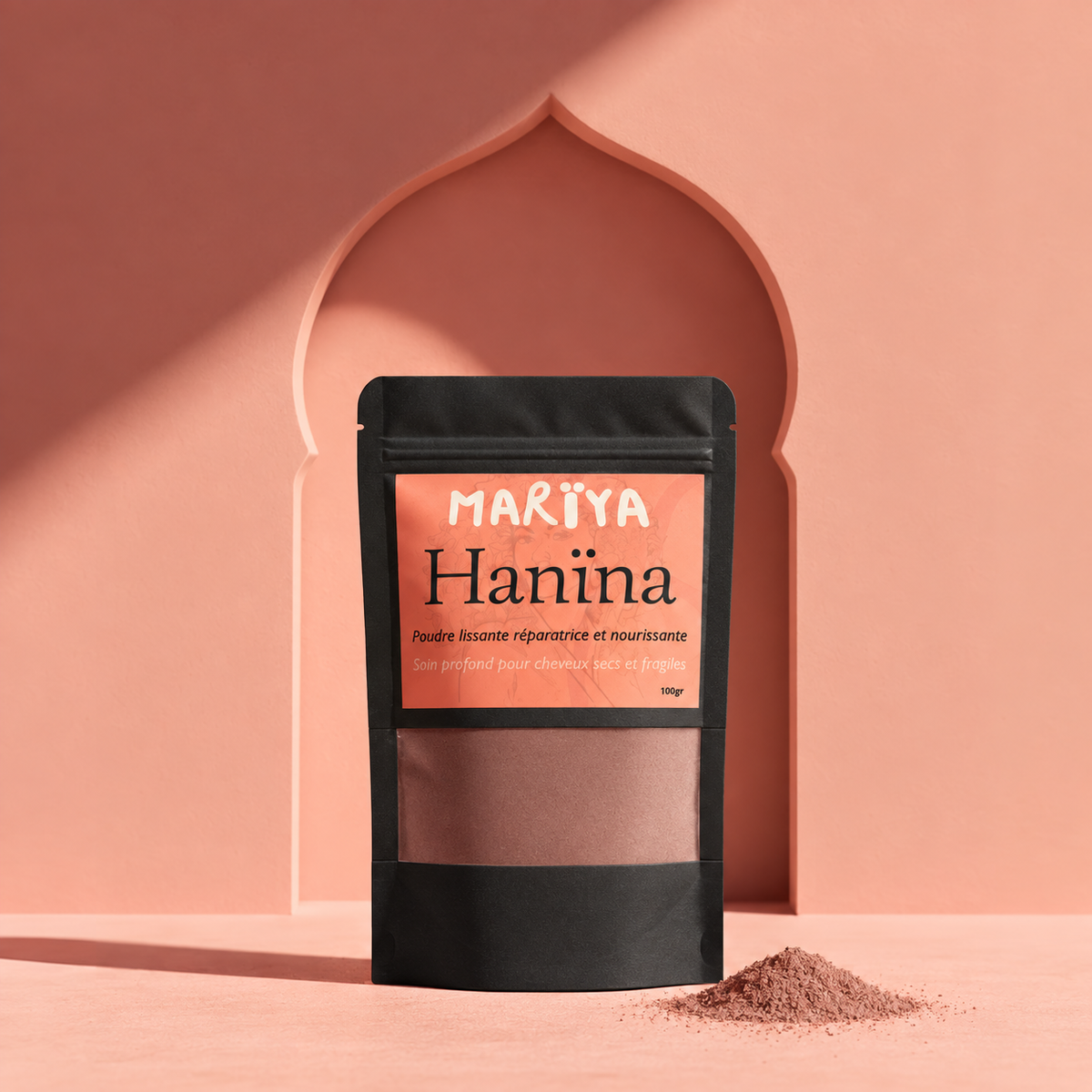 Sachet noir HANÏNA, étiquette corail et poudre brune mauve devant une arcade.